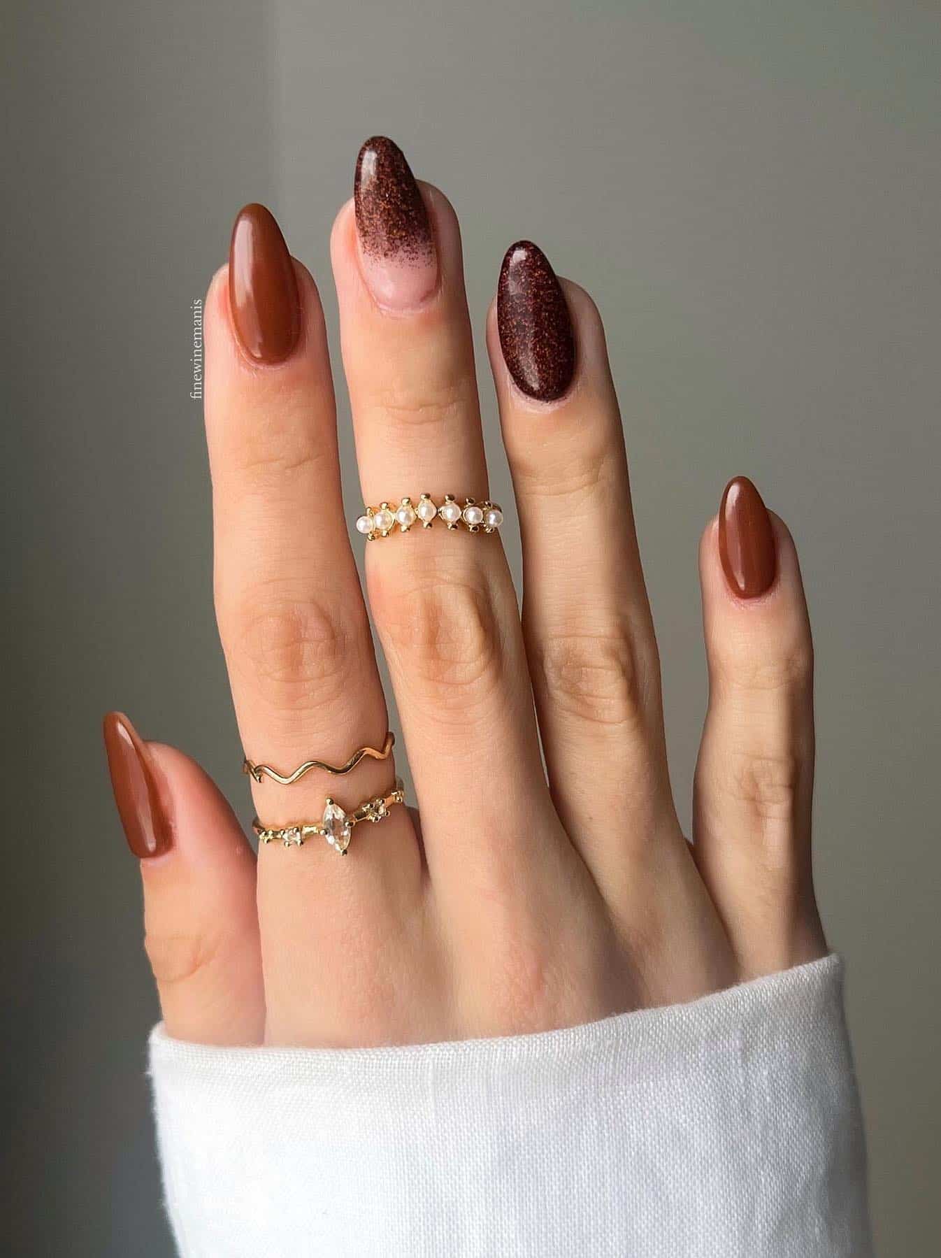 a hand with glossy brown and brown glitter nails with a nude and brown glitter ombre accent nail